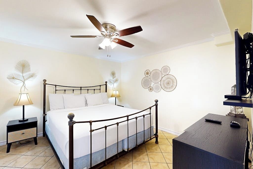 Ein Schlafzimmer mit Bett, Nachttisch, Schreibtisch, Deckenventilator und Wanddekoration.