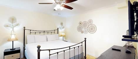 Ein Schlafzimmer mit Bett, Nachttisch, Schreibtisch, Deckenventilator und Wanddekoration.