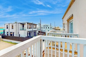A balcony with a white railing overlooking a street with buildings, including a structure labeled '2700 ARENA'. - Casa Emilio II Condominiums 201C (South Padre Island)