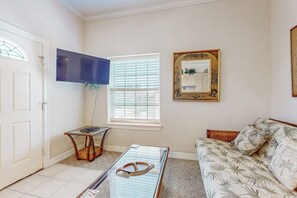 Un salon comprenant un canapé, une table basse, un téléviseur et une fenêtre avec des stores.