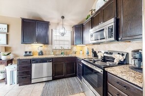 A modern kitchen with dark wood cabinets, stainless steel appliances, and a granite countertop. - Aries Chateau - Private Pool, Half Block to Beach (South Padre Island)