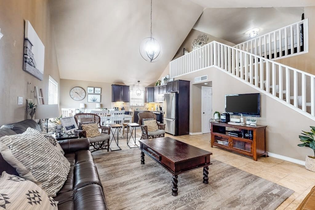 Un vaste salon doté d’un canapé en cuir marron foncé, d’une table basse en bois et d’un escalier avec des rampes blanches menant à un niveau supérieur.