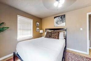 A bedroom with a bed, a ceiling fan, a window with blinds, a wall-mounted picture, and a door. - Aries Chateau - Private Pool, Half Block to Beach (South Padre Island)