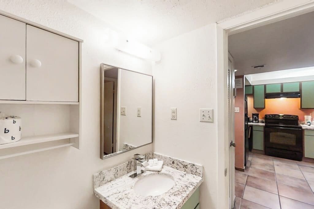 A bathroom with a sink, mirror, and toilet paper dispenser.