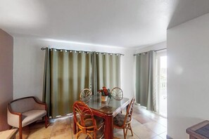 A dining area with a glass-top table, four chairs, a vase with flowers, and curtains. - Gulfview I #207 - Bay Views, Pool, Walk to Beach (South Padre Island)