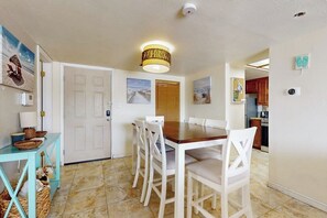Een eethoek met een houten tafel en witte stoelen, een plafondlamp en een deur naar een andere kamer.