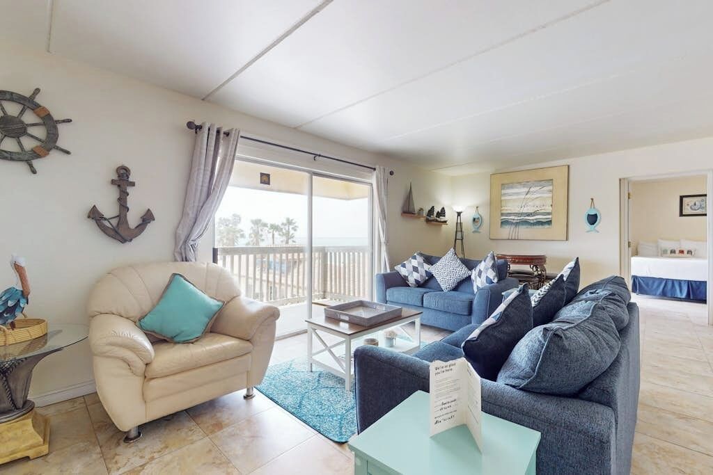 A living room with a beige sofa, a blue sofa, a coffee table, and nautical decor including an anchor and a ship's wheel.