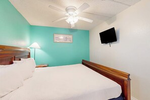 A bedroom with a bed, a ceiling fan, a wall-mounted TV, and a bedside lamp. - Florence Condominiums #707 (South Padre Island)