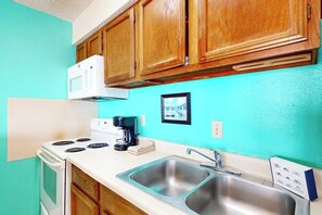 A kitchen with wooden cabinets, a white stove, a microwave, a coffee maker, and a sink. - Florence Condominiums #707 (South Padre Island)