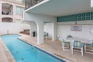 A swimming pool area with a table and chairs, a sign, and a balcony. - Florence Condominiums #707 (South Padre Island)
