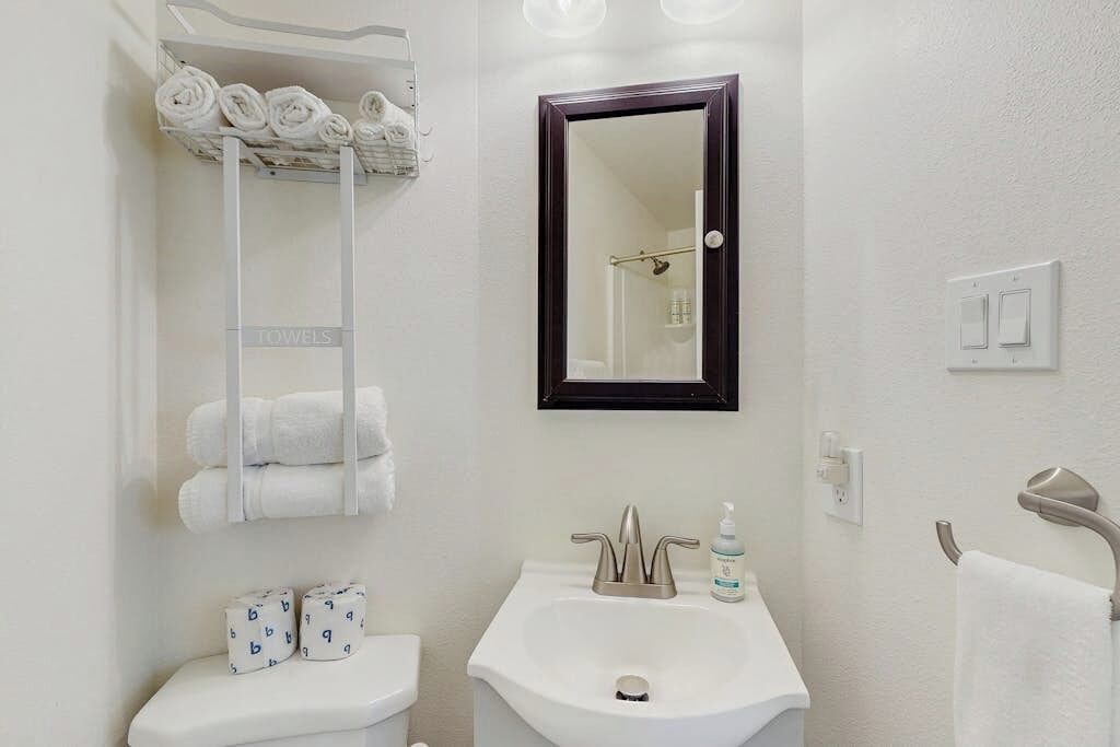 A bathroom with a white sink, a mirror, and a towel rack with rolled towels.