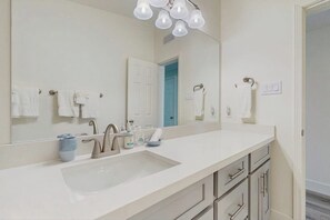 A bathroom with a large mirror, a white sink, and a towel rack. - Seaside Escape - Ocean View, Yard, Steps to Sand (Galveston)