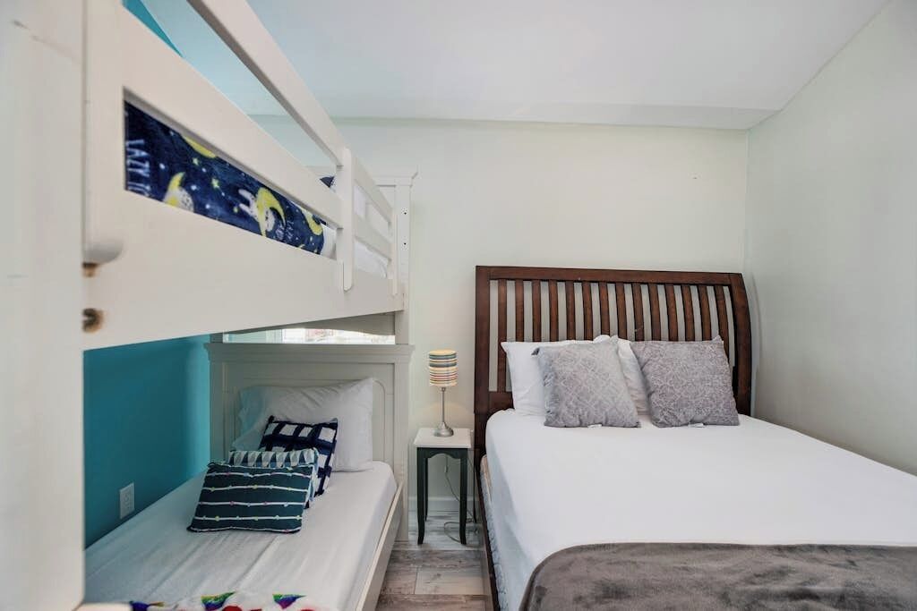 Une chambre avec un lit superposé, un lit simple et une table de chevet avec une lampe.