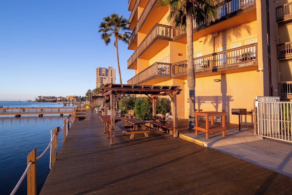 A wooden deck with picnic tables and a pergola, overlooking a body of water.