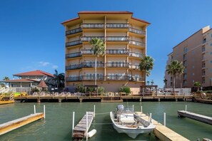 A multi-story hotel with balconies, a dock with a boat, and palm trees. - Galleon Bay Condominiums #207 (South Padre Island)