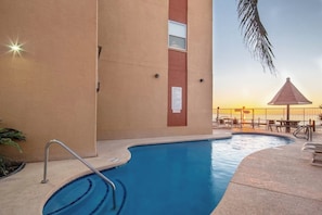 A swimming pool with a metal ladder, a palm tree, and a sunset in the background. - Galleon Bay Condominiums #207 (South Padre Island)