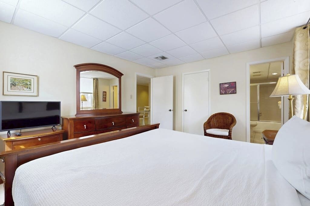 A hotel room with a large bed, a television, a dresser, a mirror, and a chair.