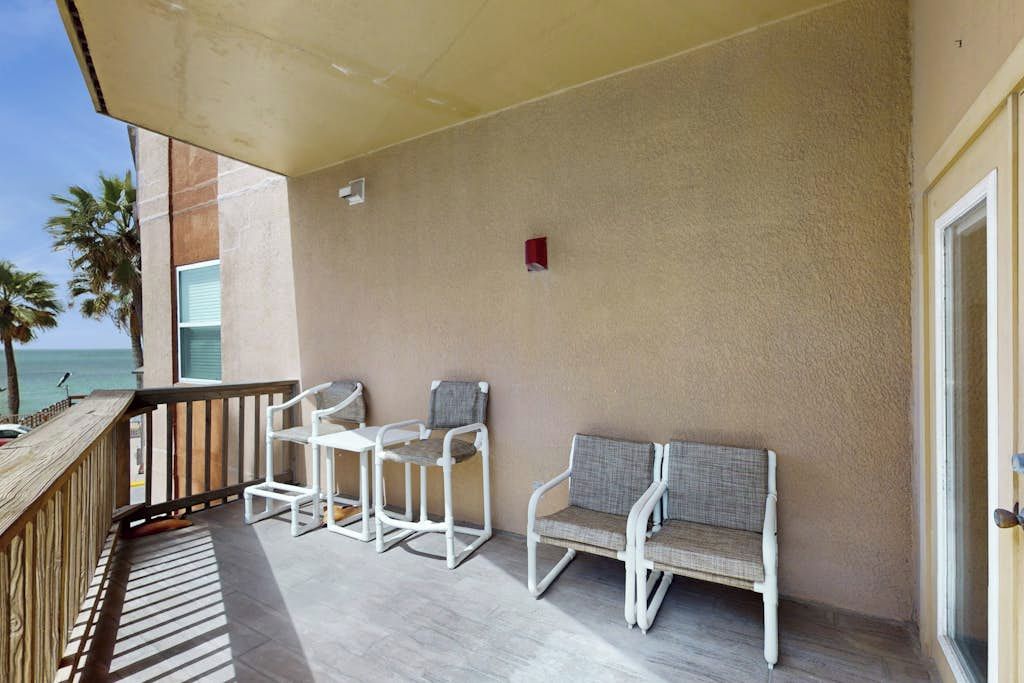 A balcony with a wooden railing, a white chair, a white table, and a white sofa.