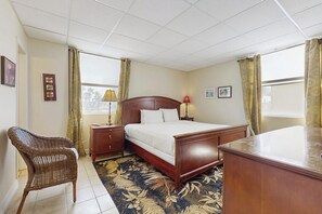 Ein Hotelzimmer mit einem Bett, einem Sessel, einem Schreibtisch und einem Fenster mit Vorhängen.