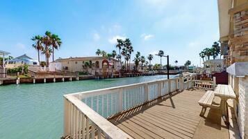 A wooden pier with a railing, a picnic table, and a building with an American flag.