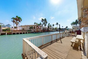 A wooden pier with a railing, a picnic table, and a building with an American flag.