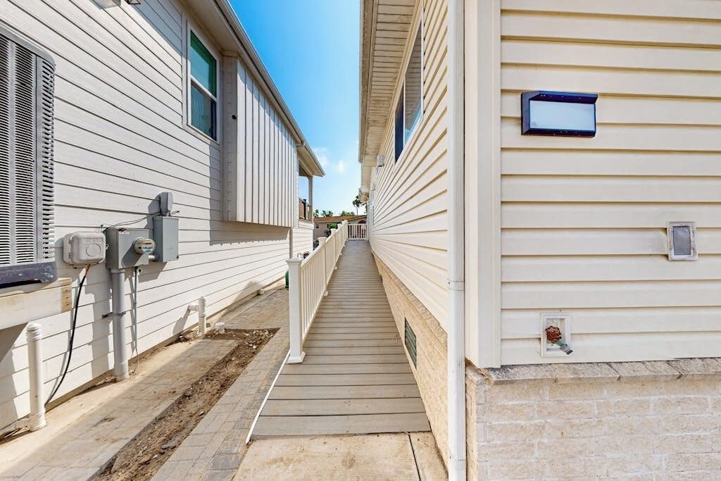 A narrow pathway between two mobile homes with a wooden deck, electrical boxes, and a small mailbox.