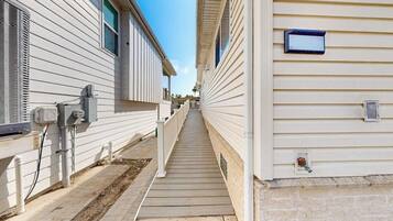 A narrow pathway between two mobile homes with a wooden deck, electrical boxes, and a small mailbox.