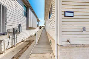 A narrow pathway between two mobile homes with a wooden deck, electrical boxes, and a small mailbox.