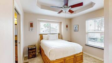 A bedroom with a wooden bed, a ceiling fan, and two windows.