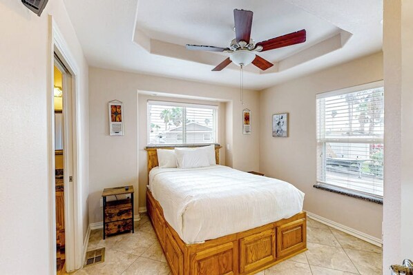 A bedroom with a wooden bed, a ceiling fan, and two windows.