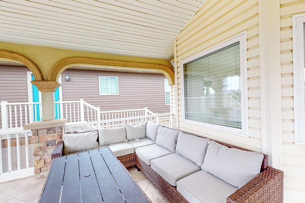 A covered patio area with a wooden table and a wicker sofa.