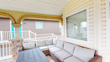 A covered patio area with a wooden table and a wicker sofa.