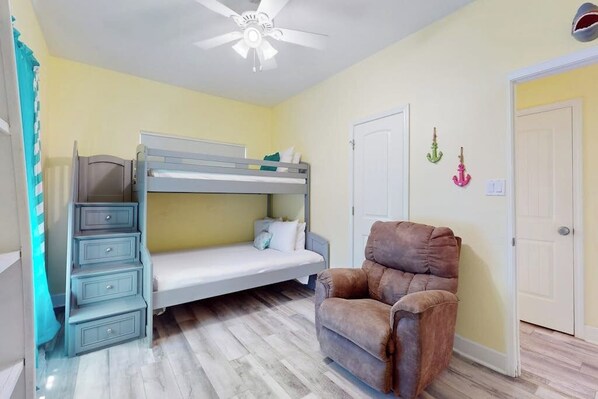 Una habitaci ón con literas, una silla, un ventilador de techo y una puerta.