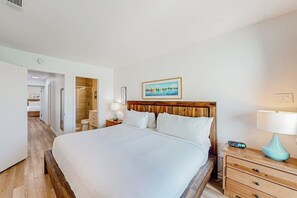 Habitació d'hotel amb un llit gran, taules de nit, un panell de fusta al capçal i un quadre a la paret, amb un bany visible a través d'una porta oberta.