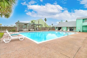 A swimming pool with lounge chairs and a covered seating area, surrounded by buildings. - Puente Vista - Aloha, Sunset on the Bay (Corpus Christi)