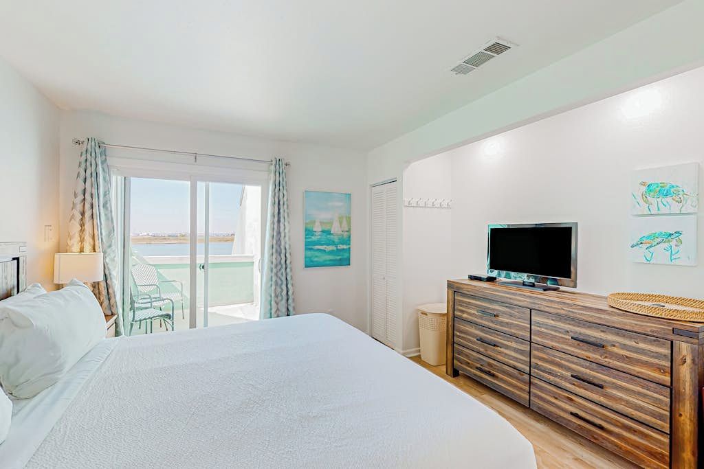 A hotel room with a bed, a TV, a wooden dresser, and a balcony with a view.