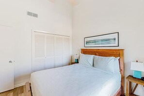 A bedroom with a bed, a nightstand, a lamp, a framed picture on the wall, and a closet. - Puente Vista - Aloha, Sunset on the Bay (Corpus Christi)