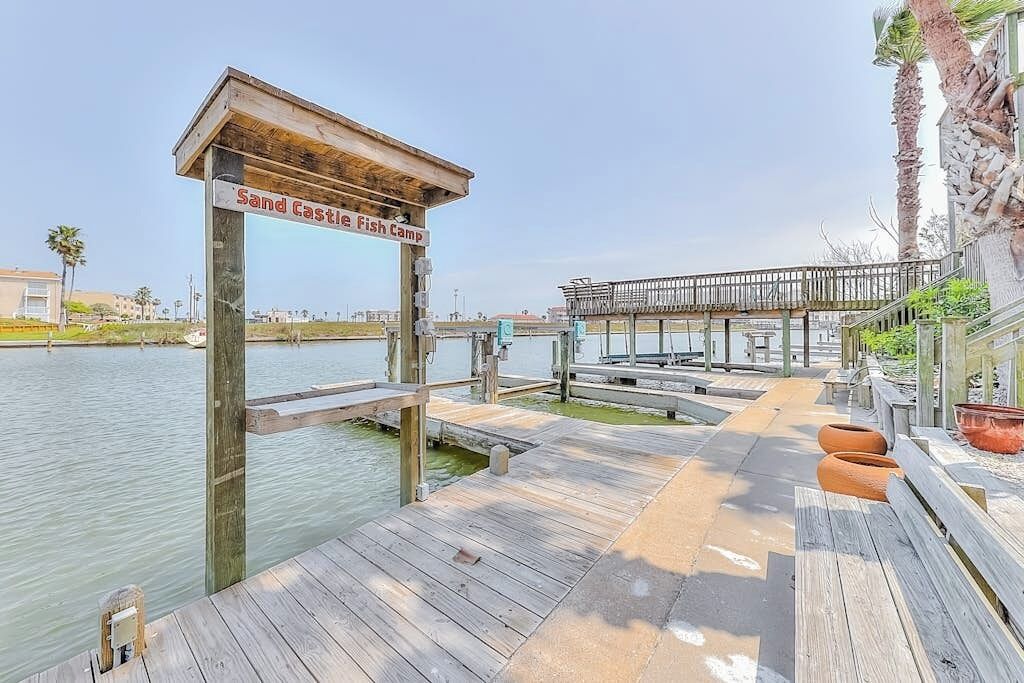Un muelle de madera que conduce a una zona de playa, con un letrero que dice 'Sand Castle Fish Camp'.