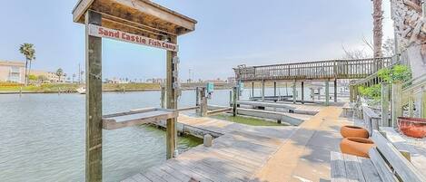 Un muelle de madera que conduce a una zona de playa, con un letrero que dice 'Sand Castle Fish Camp'.