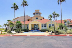 A building with a central entrance, a small tower, and a red roof. - Beach Club 326 - Pool, 2 Blocks to Beach, Dogs OK (Corpus Christi)