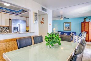 Una cucina moderna con frigorifero, tavolo da pranzo con sedie e un angolo living con divano e una pianta.