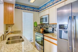 A kitchen with stainless steel appliances, a double sink, and a tiled backsplash. - Puente Vista 119 - Waterfront, Bay Views & Pool (Corpus Christi)