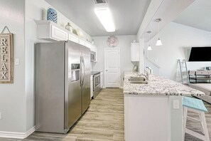 A modern kitchen with a central island, stainless steel appliances, and a white color scheme. - Nemo Cay - Mermaids Splash (Corpus Christi)