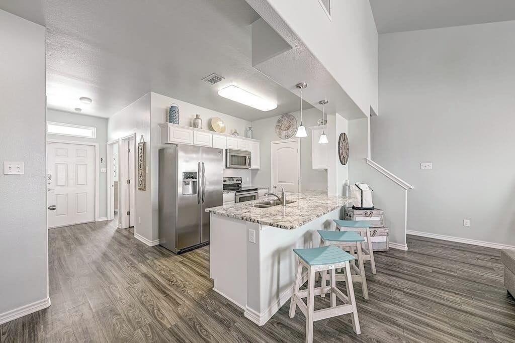 A modern kitchen with a central island, stainless steel appliances, and a staircase leading to another level.