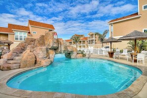 A swimming pool with a rock feature, surrounded by lounge chairs and umbrellas. - Shark's Key  -Winter/Snowbird Friendly (Port Aransas)