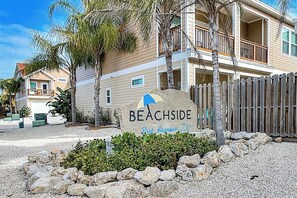 Ein Strandgrundstück namens Beachside in Port Aransas, TX, mit einem Schild, einem Holzzaun und einem Kiesbereich mit Steinen und Sträuchern.