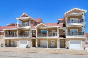 Un immeuble résidentiel à plusieurs étages, doté de balcons, de portes de garage et surplombant un ciel dégagé.
