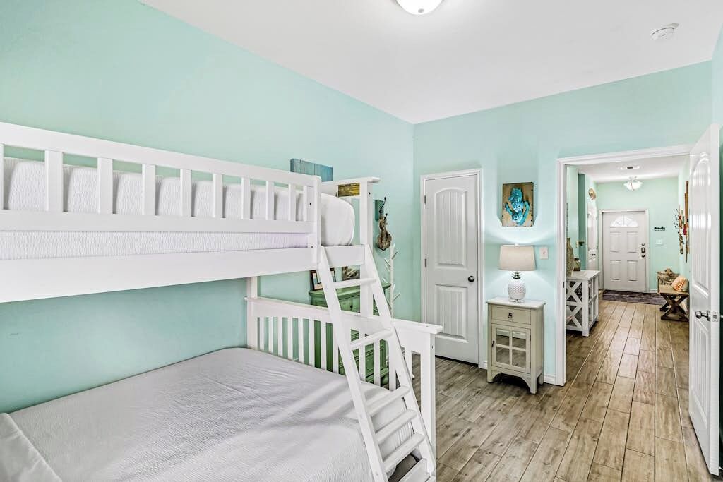 Ein Zimmer mit Etagenbetten, einer Tür, einem kleinen Tisch mit Lampe und einem zur nächsten Tür führenden Gang.
