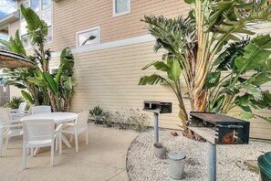Une terrasse avec une table et des chaises blanches, entourée de plantes tropicales et agrémentée d’une boîte aux lettres.