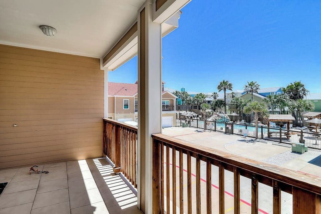 A balcony with a view of a pool area, including a pool, lounge chairs, and palm trees.